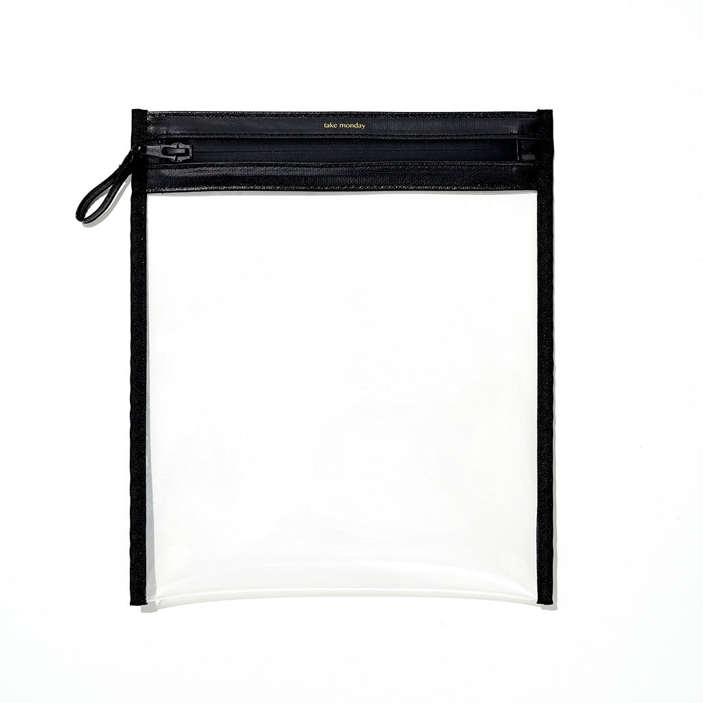 Product photograph of a rectangular clear vinyl pouch featuring a black top zipper with a black pull loop and gold take monday branding on a crisp white studio background