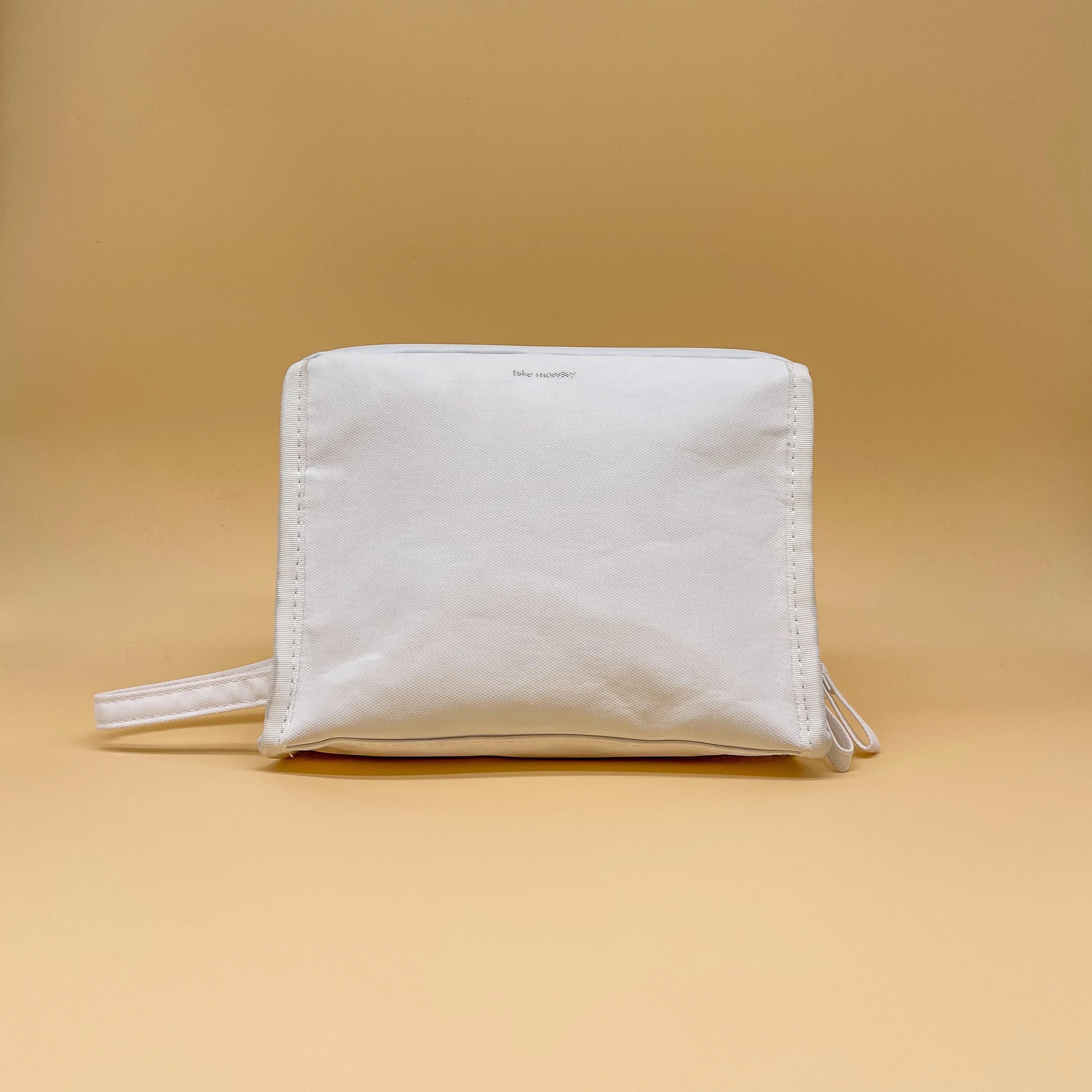 Take Monday white textured rectangular pouch featuring a subtle logo, prominent vertical stitching, and a side loop handle on a clean tan studio background